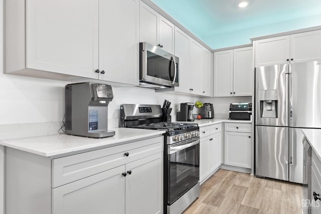 kitchen with white cabinetry, appliances with stainless steel finishes, light stone countertops, and light hardwood / wood-style floors