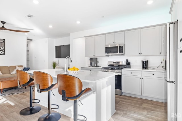 kitchen featuring white cabinetry, appliances with stainless steel finishes, a center island with sink, and a kitchen breakfast bar