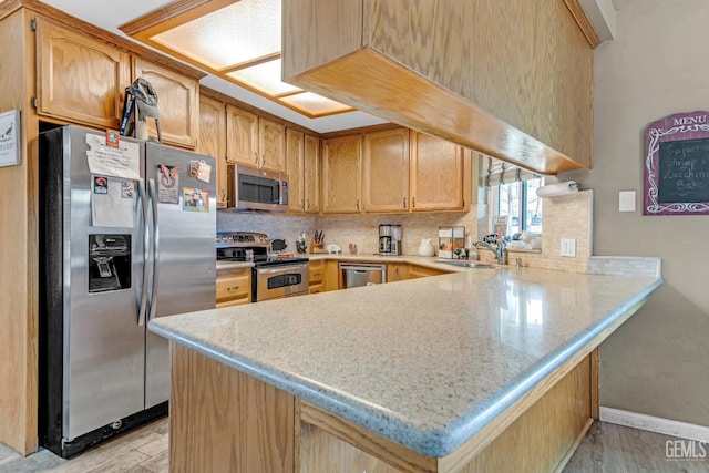 kitchen featuring kitchen peninsula, appliances with stainless steel finishes, tasteful backsplash, sink, and light hardwood / wood-style floors