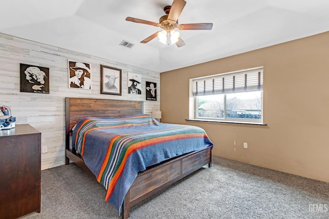 carpeted bedroom with ceiling fan and wood walls