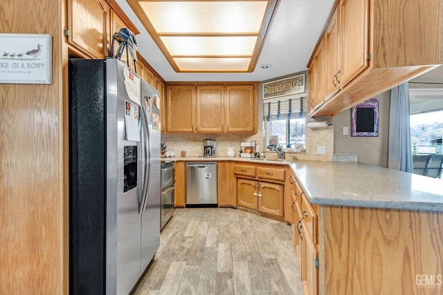 kitchen featuring sink, tasteful backsplash, kitchen peninsula, appliances with stainless steel finishes, and light wood-type flooring