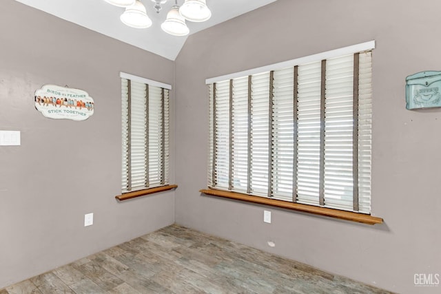 unfurnished room with light wood-type flooring, vaulted ceiling, and an inviting chandelier