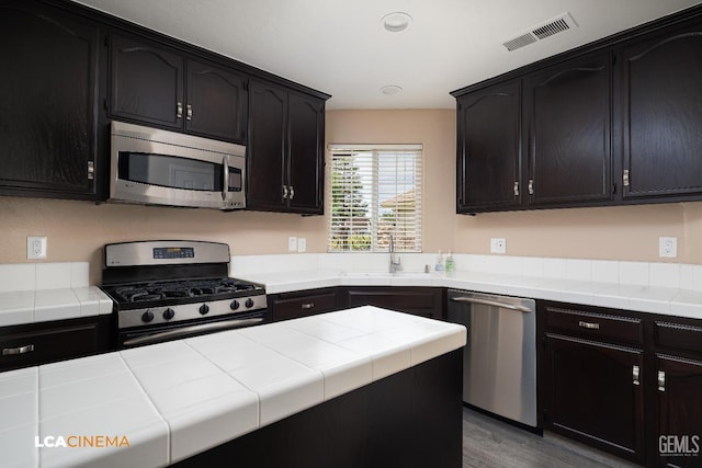 5502 White Pine Way, Bakersfield, CA 93313 - kitchen with appliances with stainless steel finishes, a sink, tile counters, dark cabinets, and wood finished floors