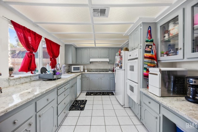 kitchen with white appliances, a sink, glass insert cabinets, and gray cabinetry