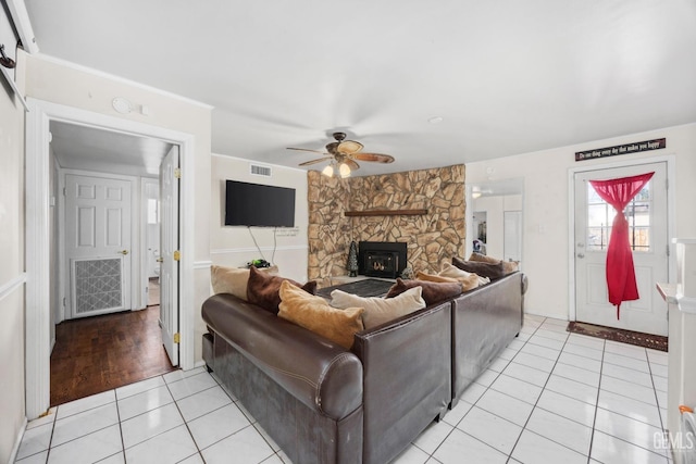 living room with visible vents, ceiling fan, a stone fireplace, and light tile patterned floors