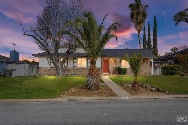 view of front of house with stone siding, fence, and a front lawn