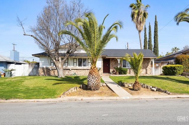 view of front of house with stone siding, fence, and a front lawn