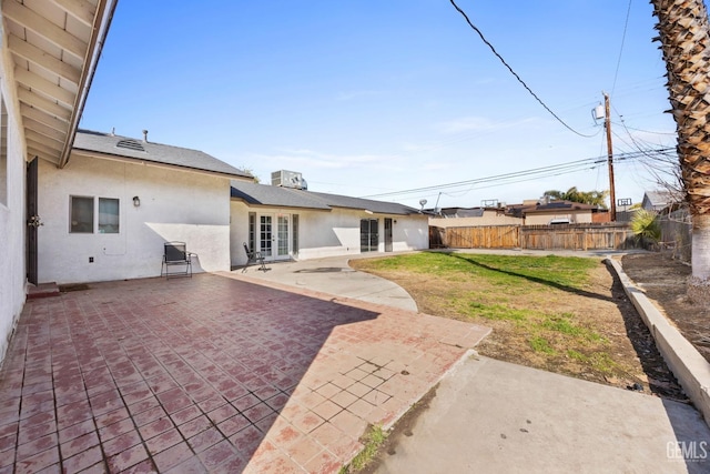 back of house with a fenced backyard, a patio, a lawn, and stucco siding