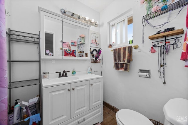 half bath with toilet, baseboards, wood finished floors, and vanity