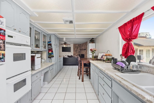 kitchen with light tile patterned floors, glass insert cabinets, open floor plan, light countertops, and gray cabinetry