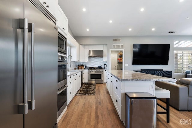 812 Mazatlan Dr, Bakersfield, CA 93314 - kitchen featuring built in appliances, wall chimney exhaust hood, open floor plan, light wood-style floors, and recessed lighting