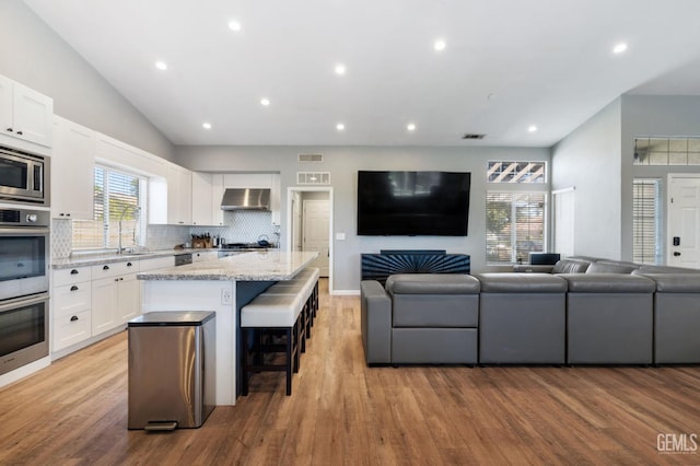 812 Mazatlan Dr, Bakersfield, CA 93314 - kitchen with wall chimney range hood, open floor plan, a kitchen island, light wood finished floors, and lofted ceiling