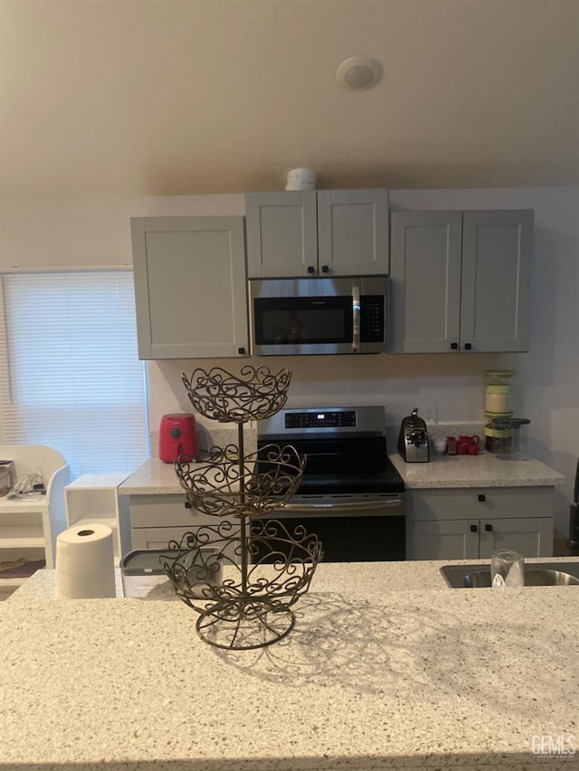 kitchen featuring gray cabinets, stainless steel appliances, light stone counters, and sink