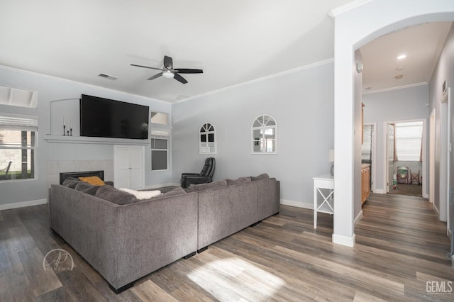 living room featuring hardwood / wood-style floors, ceiling fan, crown molding, and a tiled fireplace