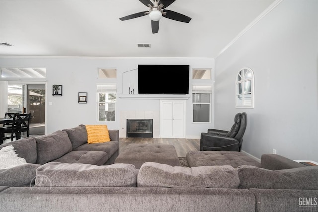 living room featuring hardwood / wood-style flooring, ceiling fan, crown molding, and a tiled fireplace