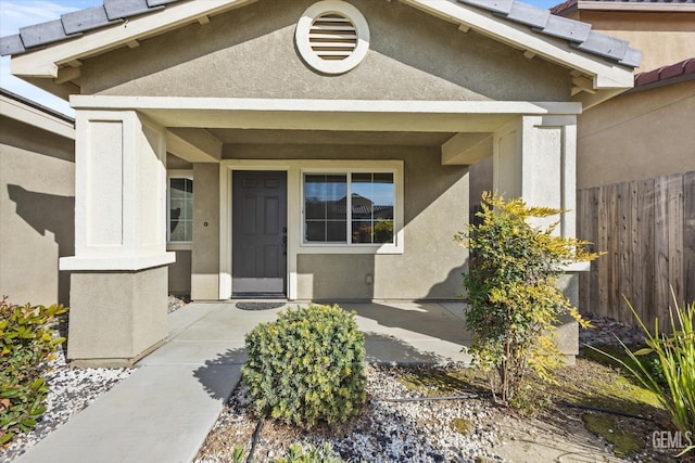 view of exterior entry with fence and stucco siding