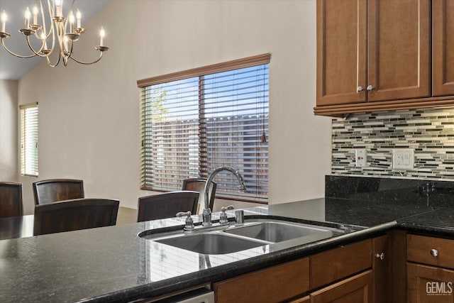 kitchen featuring pendant lighting, backsplash, an inviting chandelier, brown cabinetry, and a sink