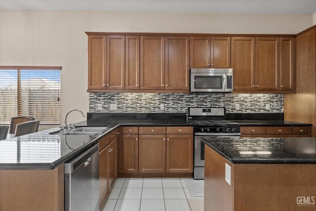 kitchen featuring light tile patterned floors, stainless steel appliances, a sink, dark stone counters, and brown cabinetry