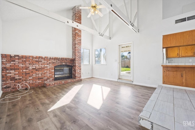 unfurnished living room featuring hardwood / wood-style floors, ceiling fan, a fireplace, and high vaulted ceiling