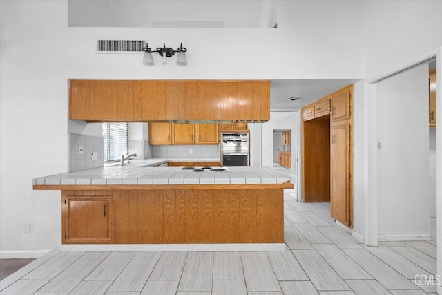 kitchen featuring backsplash, kitchen peninsula, tile countertops, and stainless steel double oven