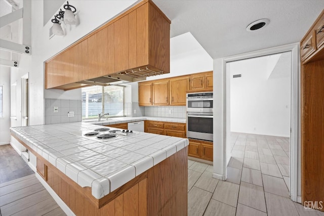 kitchen featuring kitchen peninsula, tasteful backsplash, white appliances, sink, and tile counters