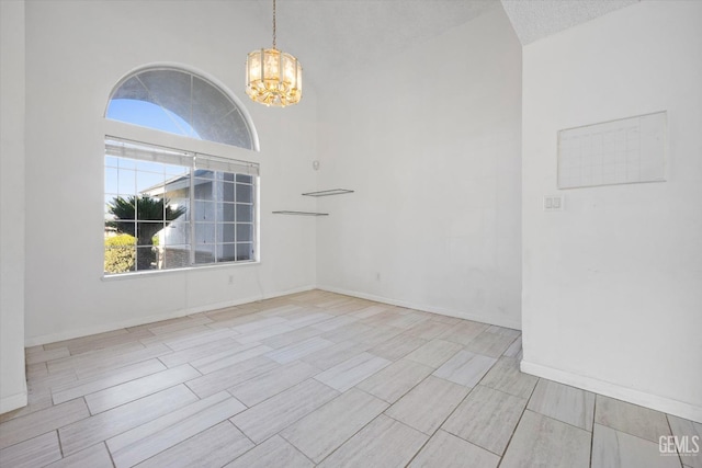 spare room featuring a notable chandelier, a healthy amount of sunlight, a towering ceiling, and a textured ceiling