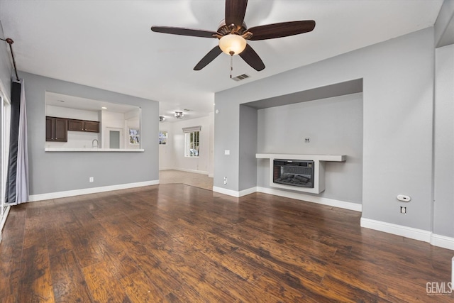 unfurnished living room with ceiling fan, visible vents, baseboards, and wood finished floors