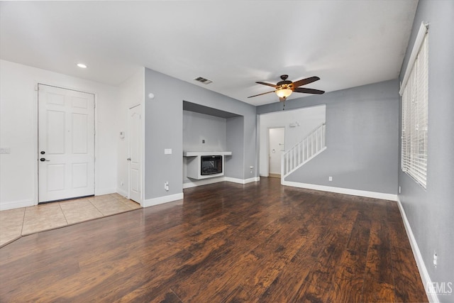 unfurnished living room with stairs, wood finished floors, baseboards, and ceiling fan