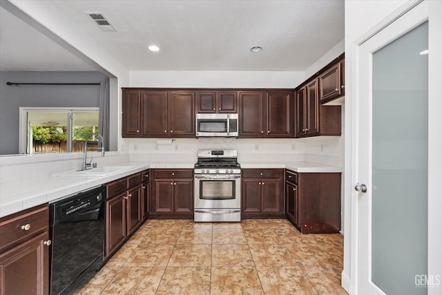 kitchen with visible vents, dark brown cabinets, tile countertops, stainless steel appliances, and a sink