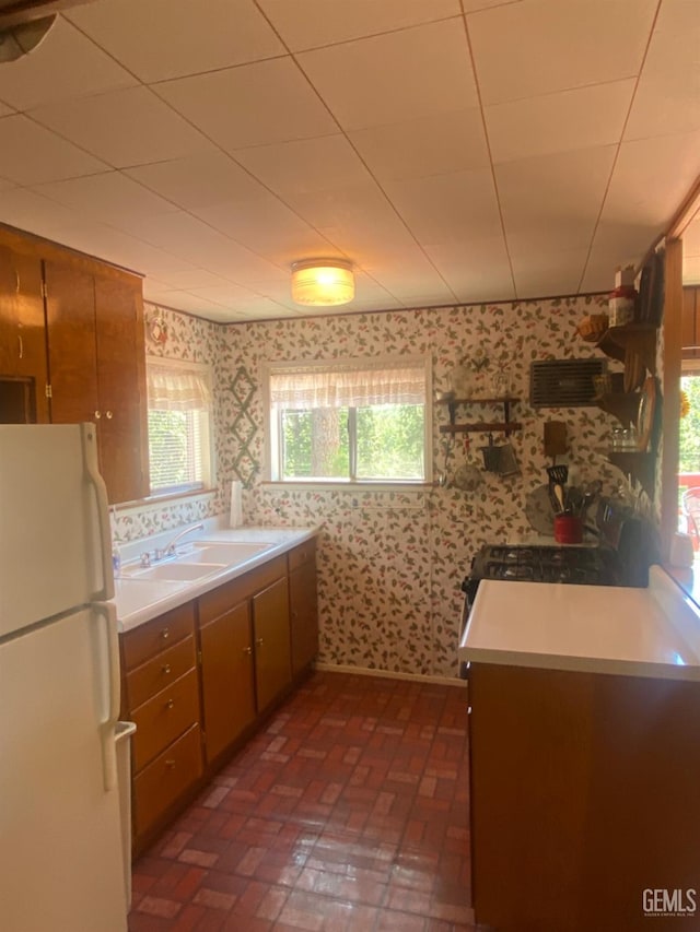 45904 Carlin Dr, Posey, CA 93260 - kitchen with freestanding refrigerator, wallpapered walls, brick flooring, brown cabinetry, and light countertops