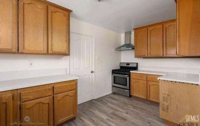 kitchen featuring light wood-type flooring, gas stove, and wall chimney range hood