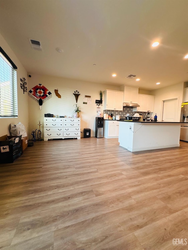 8410 Avon St, Bakersfield, CA 93314 - kitchen with dark countertops, stainless steel fridge, white cabinets, light wood-style floors, and under cabinet range hood