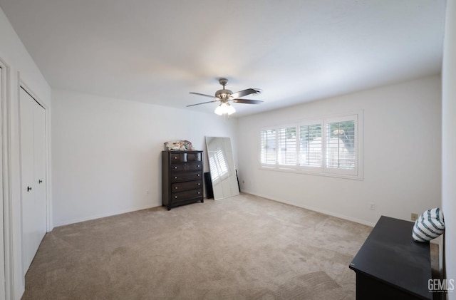 bedroom with light carpet, ceiling fan, a closet, and baseboards