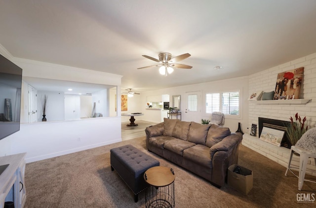 living room featuring ceiling fan, carpet flooring, baseboards, ornamental molding, and a brick fireplace