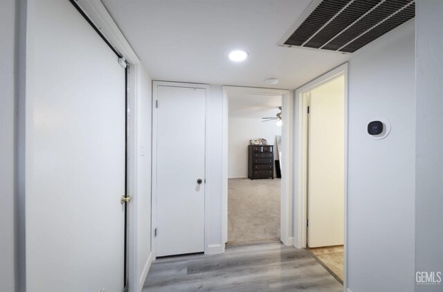 hallway featuring light wood finished floors, visible vents, and recessed lighting