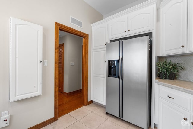 kitchen featuring stainless steel fridge with ice dispenser, light tile patterned floors, tile countertops, and white cabinetry