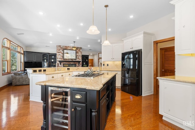 kitchen featuring black fridge with ice dispenser, a large island with sink, decorative light fixtures, white cabinetry, and wine cooler