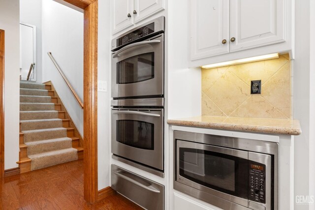 kitchen with backsplash, stainless steel appliances, white cabinetry, and dark wood-type flooring