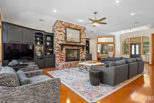 living room with ceiling fan, light hardwood / wood-style floors, lofted ceiling, and a brick fireplace