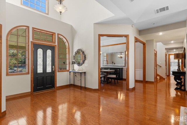 foyer featuring a towering ceiling, hardwood / wood-style flooring, an inviting chandelier, and a healthy amount of sunlight