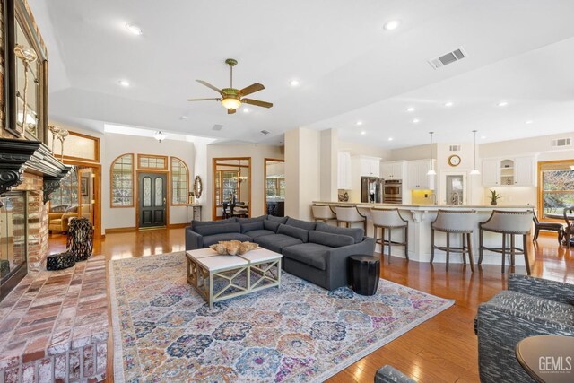 living room featuring ceiling fan, light hardwood / wood-style flooring, and a brick fireplace