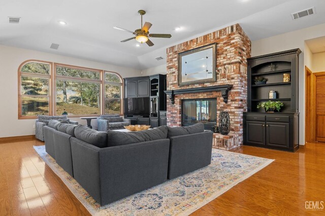 living room featuring light wood-type flooring, a brick fireplace, ceiling fan, and lofted ceiling