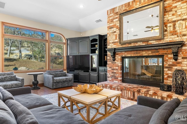 living room featuring ceiling fan, light hardwood / wood-style floors, lofted ceiling, and a brick fireplace