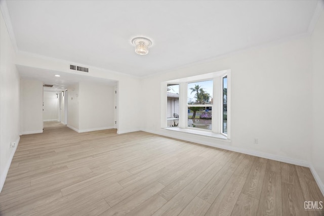 empty room with ornamental molding, light wood-type flooring, visible vents, and baseboards