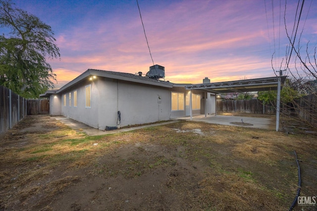 back of property at dusk featuring a patio, a fenced backyard, and stucco siding