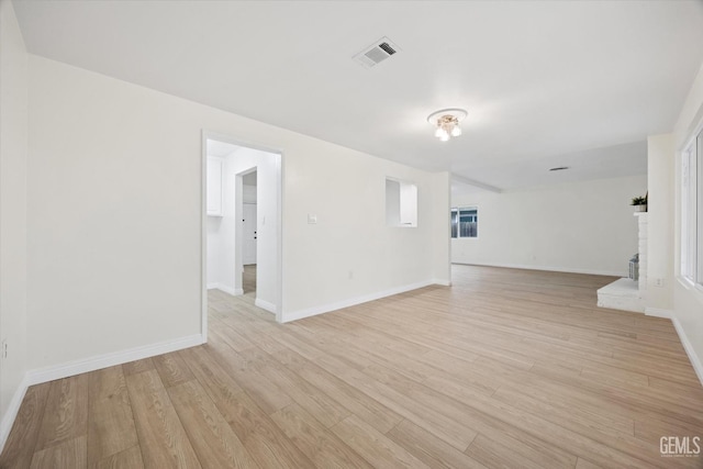 unfurnished room featuring light wood-style floors, baseboards, a fireplace, and visible vents