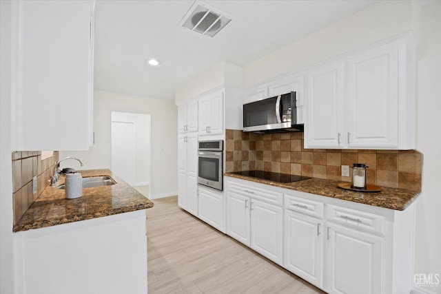 kitchen featuring stainless steel appliances, visible vents, white cabinets, a sink, and dark stone countertops