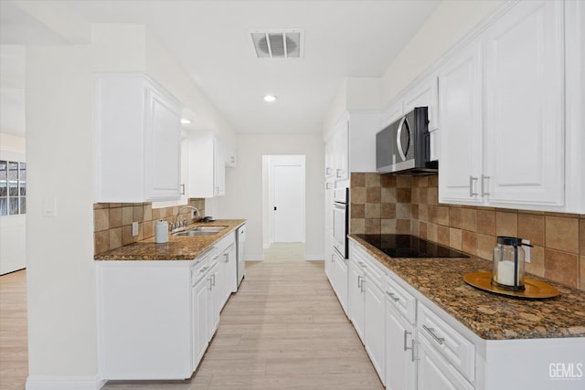 kitchen with white appliances, visible vents, dark stone countertops, white cabinetry, and a sink