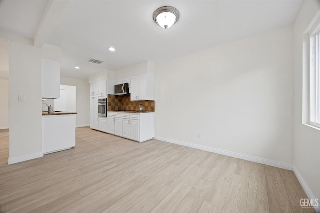 kitchen with light wood finished floors, stainless steel appliances, dark countertops, visible vents, and decorative backsplash