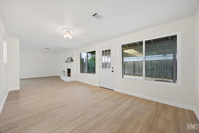 unfurnished room featuring light wood-style flooring, a fireplace, visible vents, and baseboards